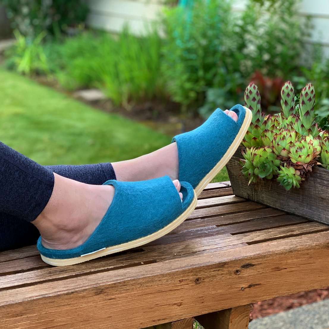 image of woman sitting back on bench wearing nootkas slip on sandals in teal - links to Sale Items  on Nootkas site